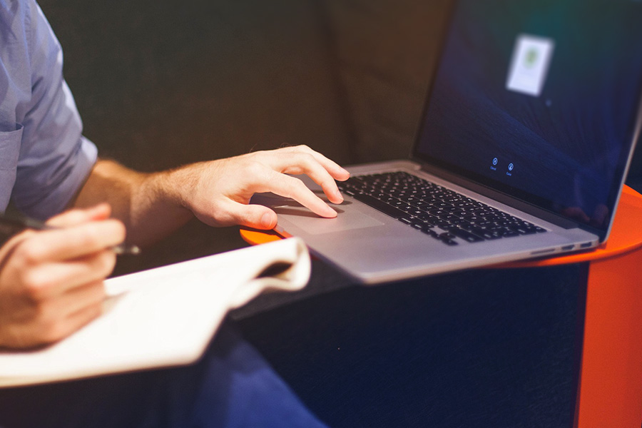 Hands typing on a laptop beside handwritten notes